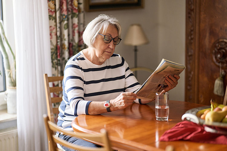 Ambulante Pflege Seniorin liest Zeitung an ihrem Küchentisch